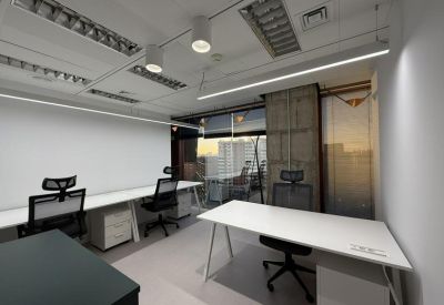 Open office area with white desks and black ergonomic chairs under linear lighting.