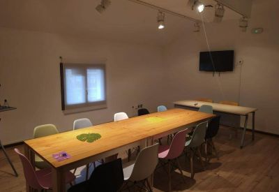 Communal space with a long wooden table and colorful modern chairs under track lighting.