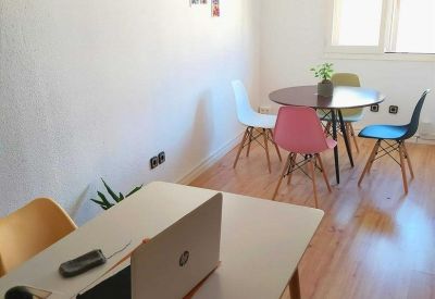 Bright workspace featuring a large white table and a smaller round table with pink and blue chairs.