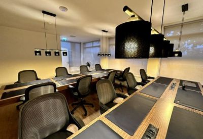 Co-working space with long wooden desks, black desk pads, and modern task lighting.