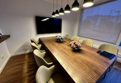 Spacious boardroom with a large wooden table, pink floral centerpieces, and a flat-screen TV.