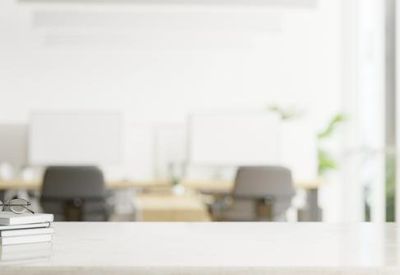 Blurry white workspace view with minimalist desks and chairs.