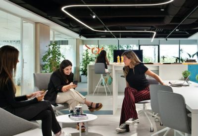 Collaborative breakout space with people sitting on modern grey chairs under a linear light fixture.