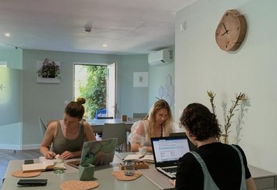 Bright coworking space with professionals working at a large shared desk near a sunny window.