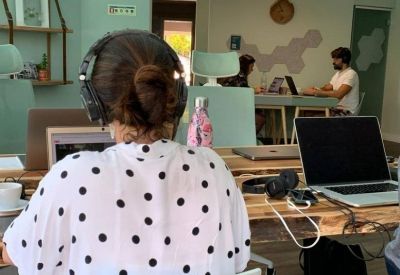 Coworking area with individuals at desks and a view into a secondary workspace through an archway.