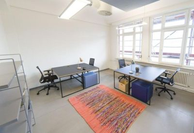 Bright office space with two large desks, ergonomic chairs, and a colorful patterned rug.