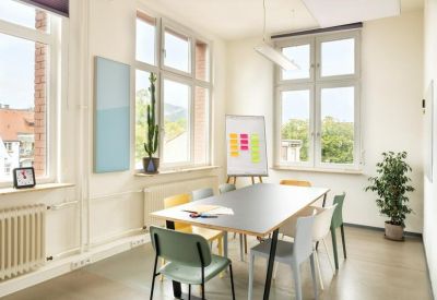 Sunny meeting room with a large table, colorful chairs, and a whiteboard.