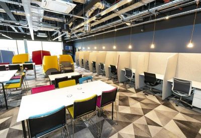 Coworking space featuring long white tables with colorful chairs and individual privacy booths.