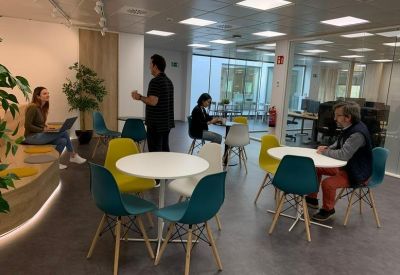 Bright coworking area with colorful teal and yellow chairs around white tables.