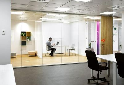 Glass-enclosed private office with a white desk and modern black chair.