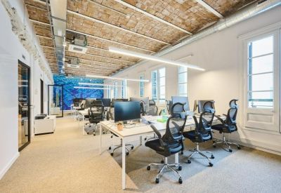 Open-plan workspace with ergonomic chairs, multiple monitors, and brick ceilings.
