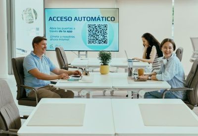 Bright coworking area with people working at desks and a large digital display.