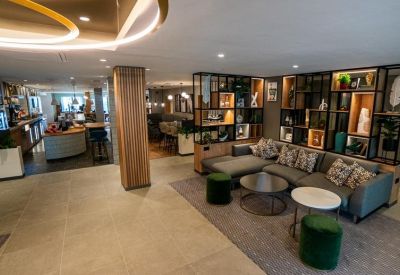 Open-plan lobby lounge with grey sectional sofas, green ottomans, and decorative shelving.