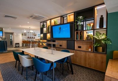 Collaborative workspace with a communal white desk and a large TV mounted on a decorative shelf.
