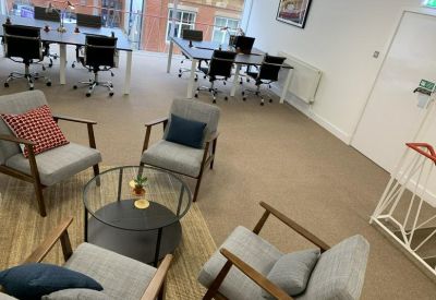 Modern breakout lounge with grey armchairs, a round coffee table, and background workstations.