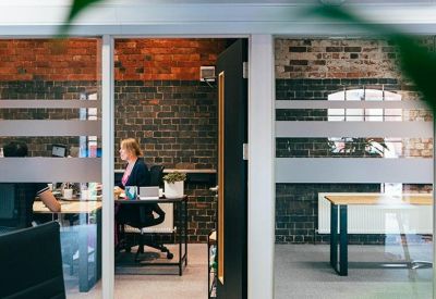 Bright glass-walled breakout area and private office spaces with industrial brick accents.