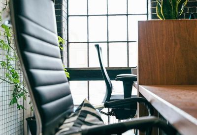 Close-up of a modern ergonomic office chair next to a wooden desk and large window.