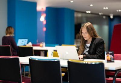 A modern coworking space with people working on laptops at communal tables.