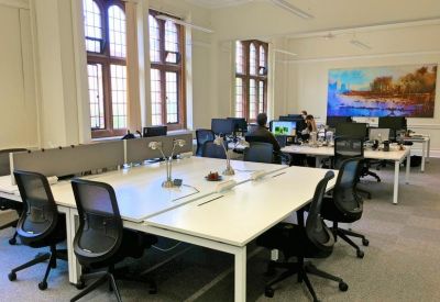 Bright open-plan office featuring white desks, ergonomic black chairs, and large arched windows.