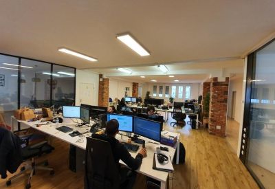 Open-plan workspace with multiple desks and wooden flooring.