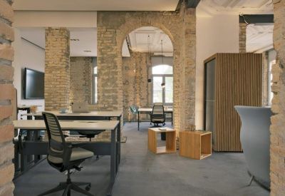 Industrial-style open-plan workspace with height-adjustable desks and rustic brick pillars.