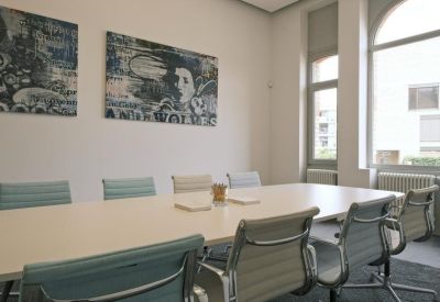 Bright meeting room with a large white table, teal office chairs, and modern wall art.
