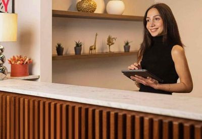 Close-up of a wooden reception desk with a marble top and a woman using a tablet.