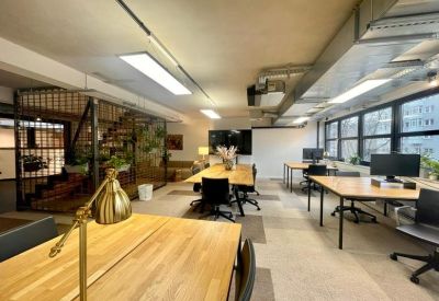 Open-plan office space with long wooden desks, ergonomic chairs, and large windows.