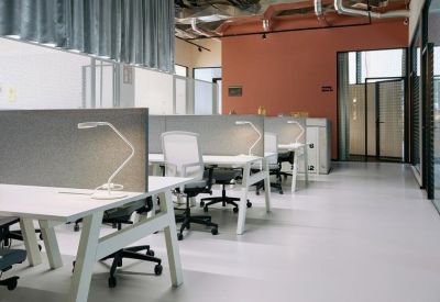 Modern open-plan office with white desks, grey dividers, and industrial ceiling details.