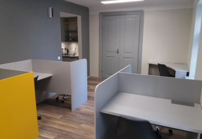 Coworking area with grey cubicle partitions and a view into a kitchenette.