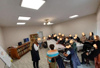 Large community room with people seated around tables for a workshop and bright overhead lighting.