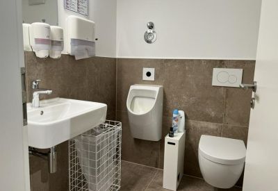 Modern restroom with dark tiling, a white sink, and a urinal.