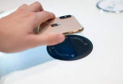 Close-up of a hand placing a smartphone on a circular wireless charging pad integrated into a desk.