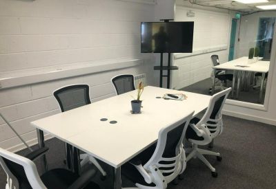 Bright meeting room with a white table, mesh chairs, and a large wall-mounted screen.