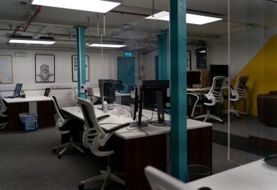 Spacious shared office with multiple white desks and teal support pillars.