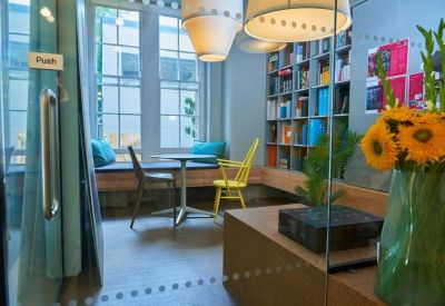 Breakout area with a built-in window bench, colorful pillows, and a yellow chair.