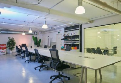 Spacious open-plan office with a long white communal desk and black ergonomic chairs.