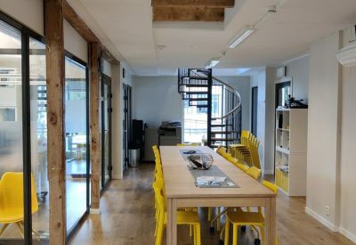 Bright coworking space with a long wooden table, yellow chairs, and a spiral staircase.