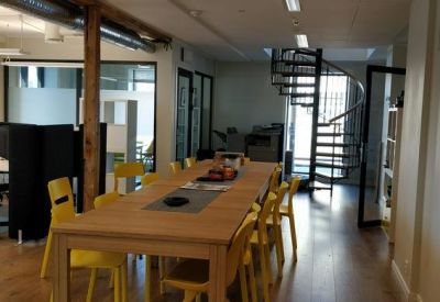 Open office area with wooden support beams and a communal wooden desk with yellow seating.