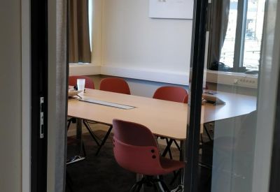 Modern meeting room featuring a light wood table and red chairs visible through a glass door.