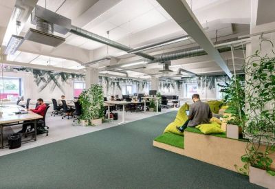 Open-plan office space featuring green carpeting, indoor plants, and tiered wooden seating areas.