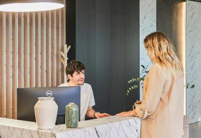 Modern reception desk with marble finish, wood-slat wall, and friendly staff member.