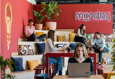 Communal lounge with tiered wooden seating, red feature walls, and indoor plants.