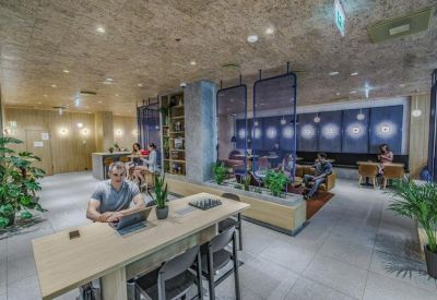 Coworking space featuring long wooden tables, indoor plants, and blue glass partitions.
