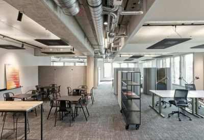 Spacious communal area with wooden tables, black chairs, and exposed ceiling pipes.