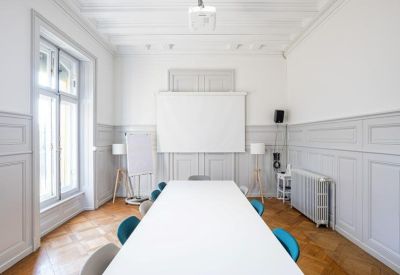 Meeting room with a long white table, teal chairs, and grey wall paneling.
