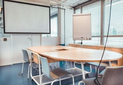 Spacious meeting room with a large oval wooden table and presentation screens.