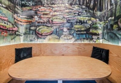 Cozy dining booth with a light wood table and a vibrant nature-themed wall mural.