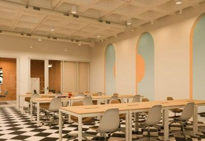 Bright open-plan workspace with light wood desks, grey ergonomic chairs, and checkered flooring.