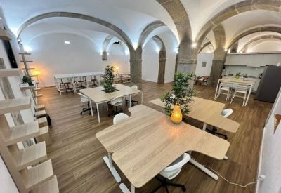 Open-plan office area with modular wooden desks, ergonomic chairs, and stone architectural pillars.